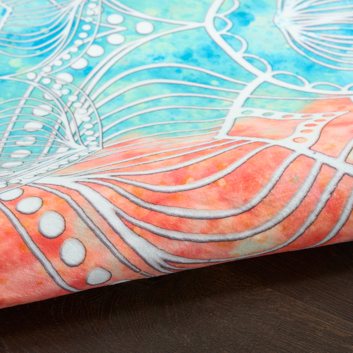 Close-up fabric with blue-teal gradient, pink edge, white metallic lines forming abstract floral/mandala pattern on wood.