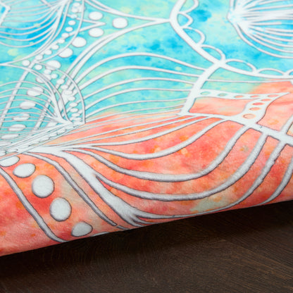 Close-up fabric with blue-teal gradient, pink edge, white metallic lines forming abstract floral/mandala pattern on wood.