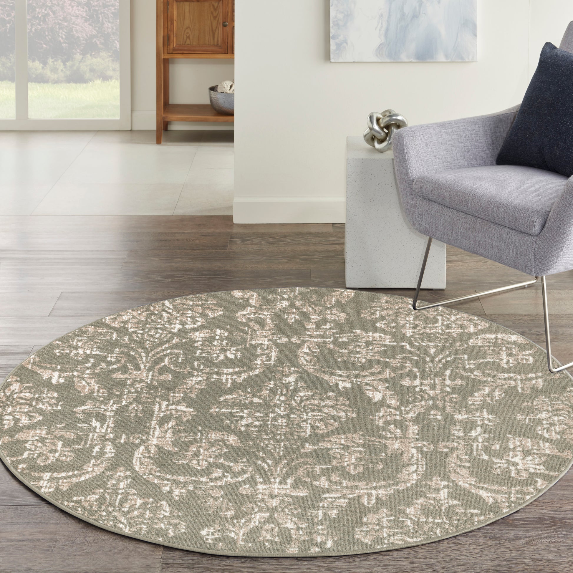 Round damask-patterned rug in muted beige on gray, modern living room with light wood floors and a gray armchair.