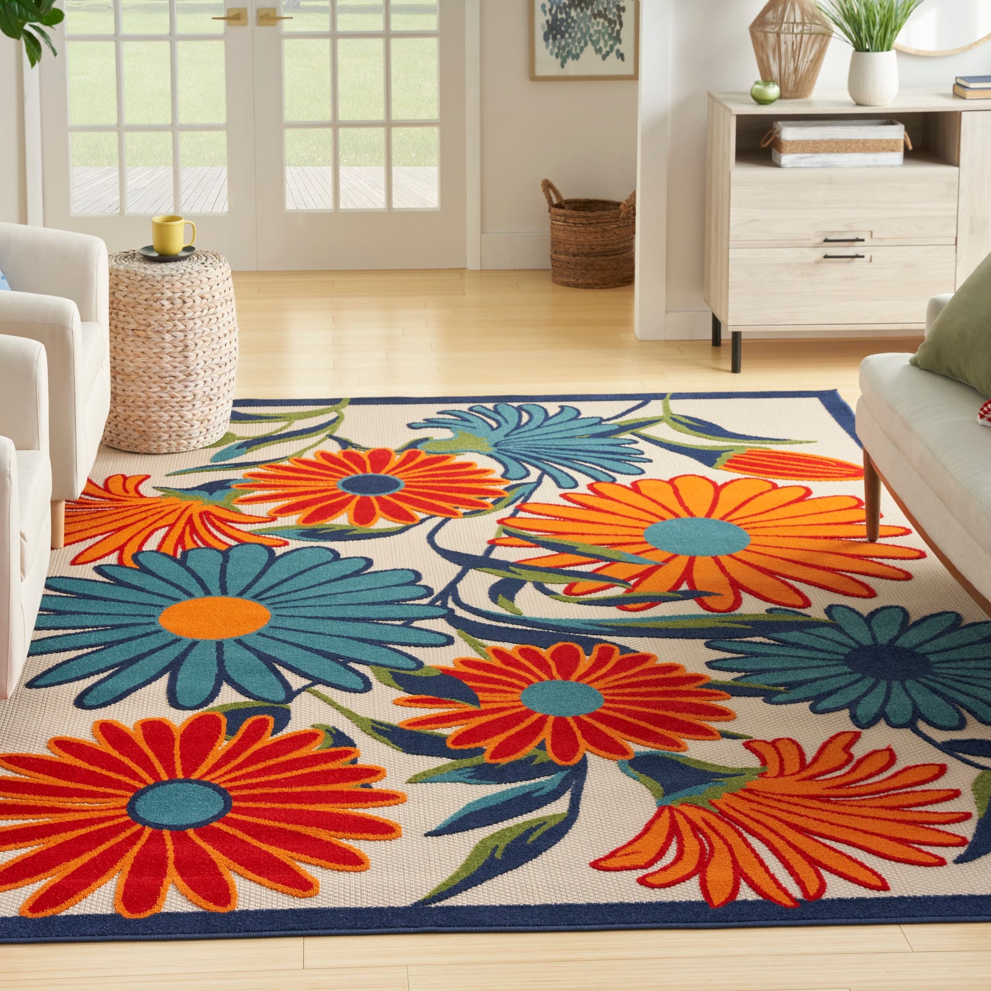 Soft woven area rug with oversized orange and blue floral pattern, cream background and navy border in a bright living room.