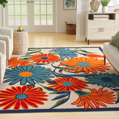 Soft woven area rug with oversized orange and blue floral pattern, cream background and navy border in a bright living room.