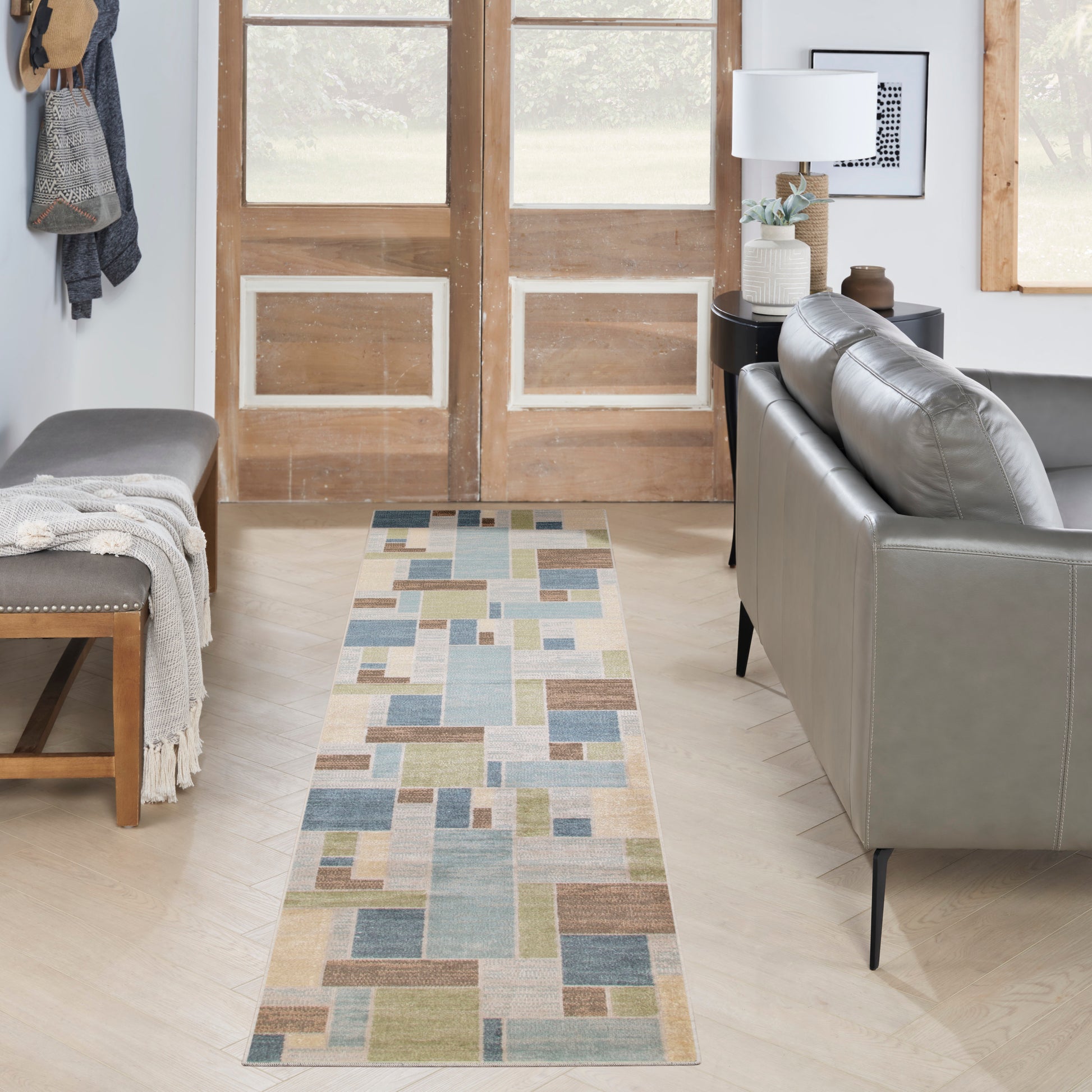 Pastel geometric patchwork rug runner in blues, greens, and beiges on light wood floor in modern living room.