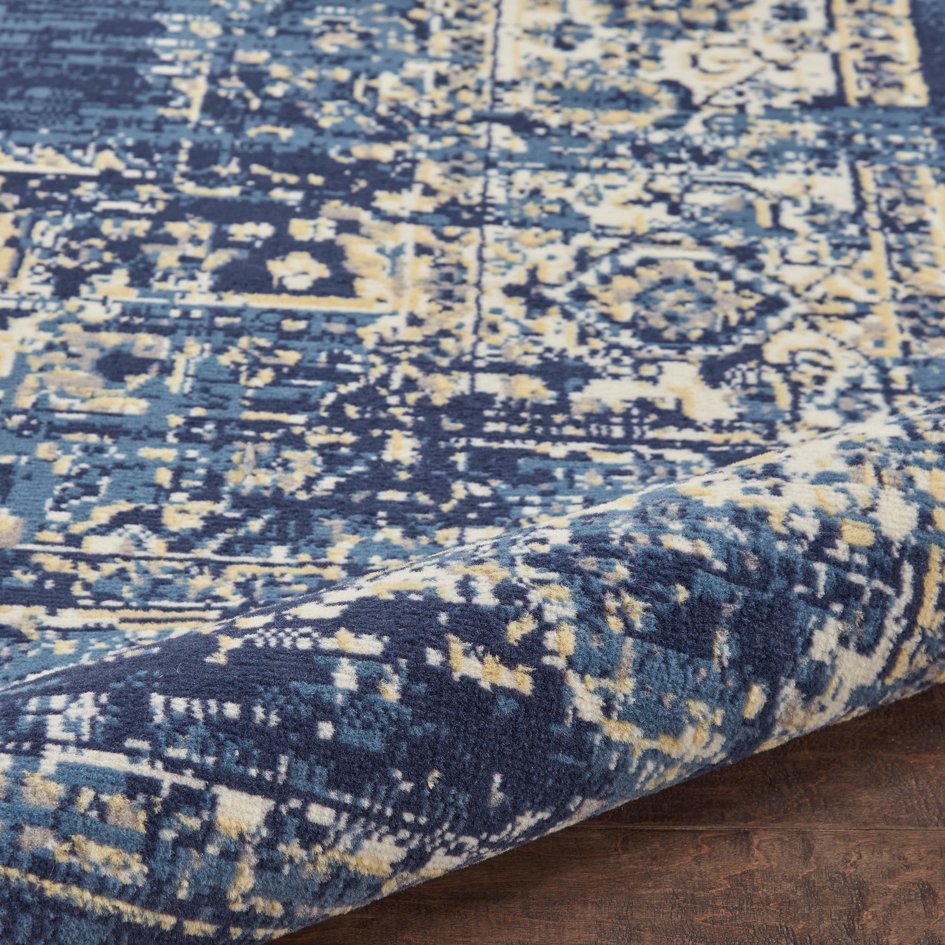 Blue & cream distressed oriental area rug with floral medallion pattern, woven texture, folded edge on wooden floor.