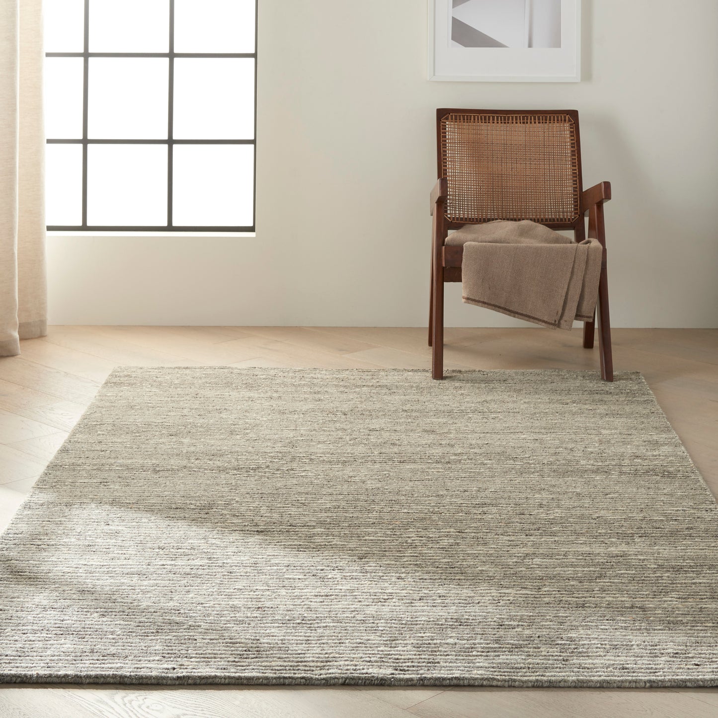 Rectangular light gray woven rug on light wood floor beside a mid-century wooden chair with a cane back and beige throw.