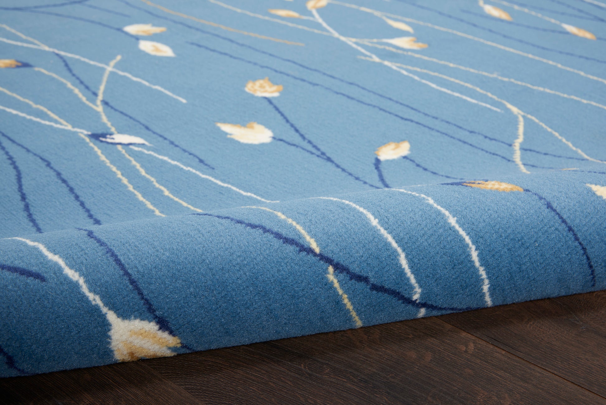 Blue rug with white wavy lines and small yellow leaf motifs, folded edge on dark wood floor.