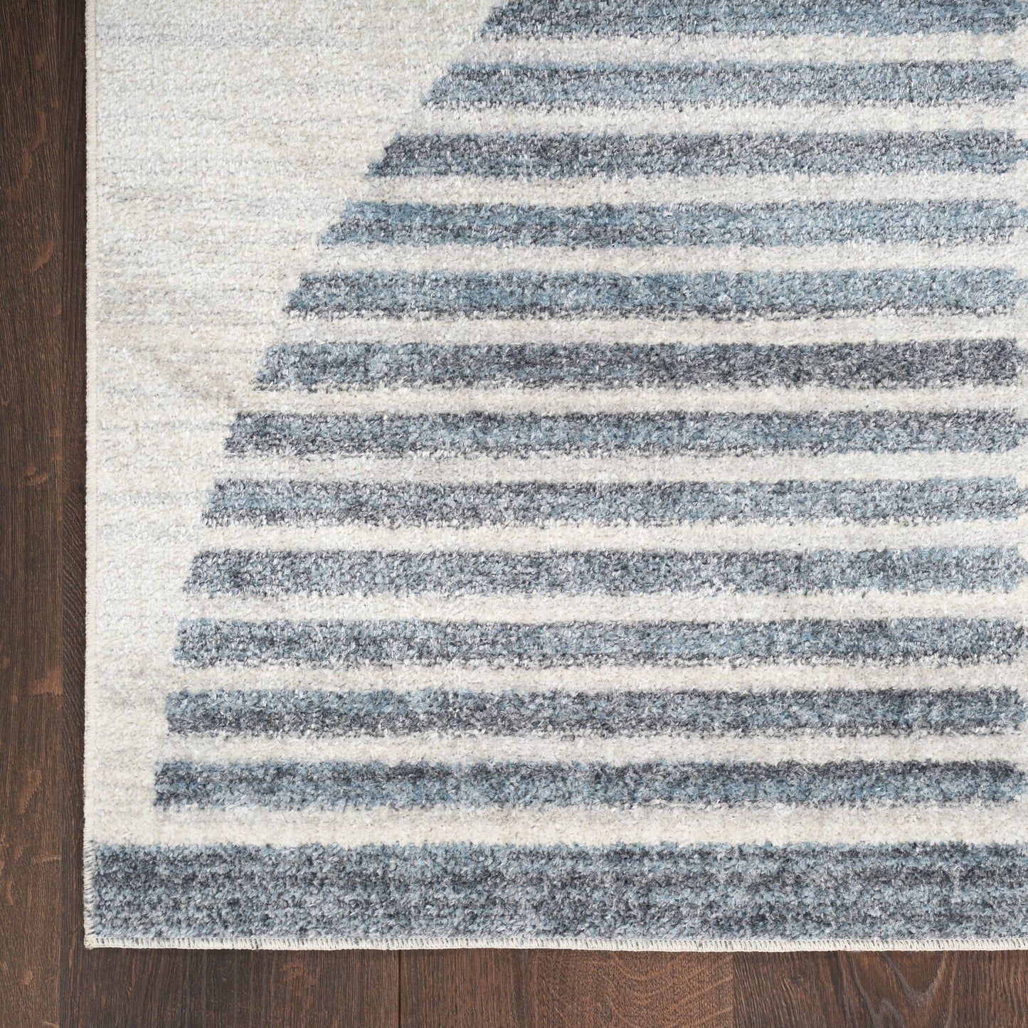 Blue and white striped area rug on dark wooden floor with curved stripe pattern.