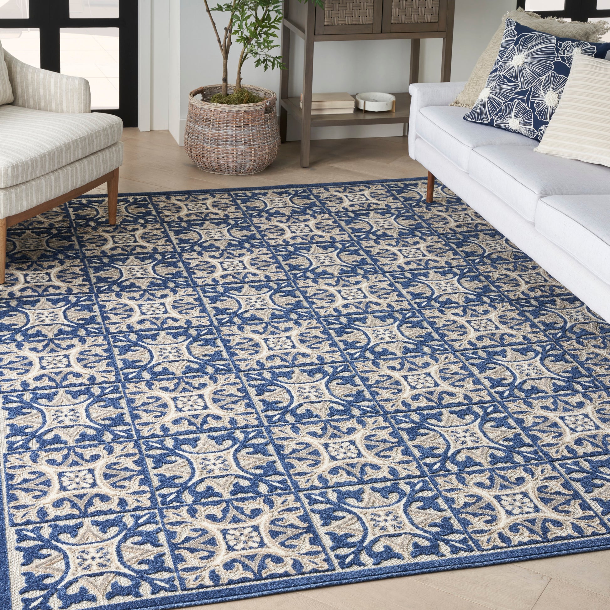 Blue and beige woven area rug with tile-like floral motifs on light wood floor.