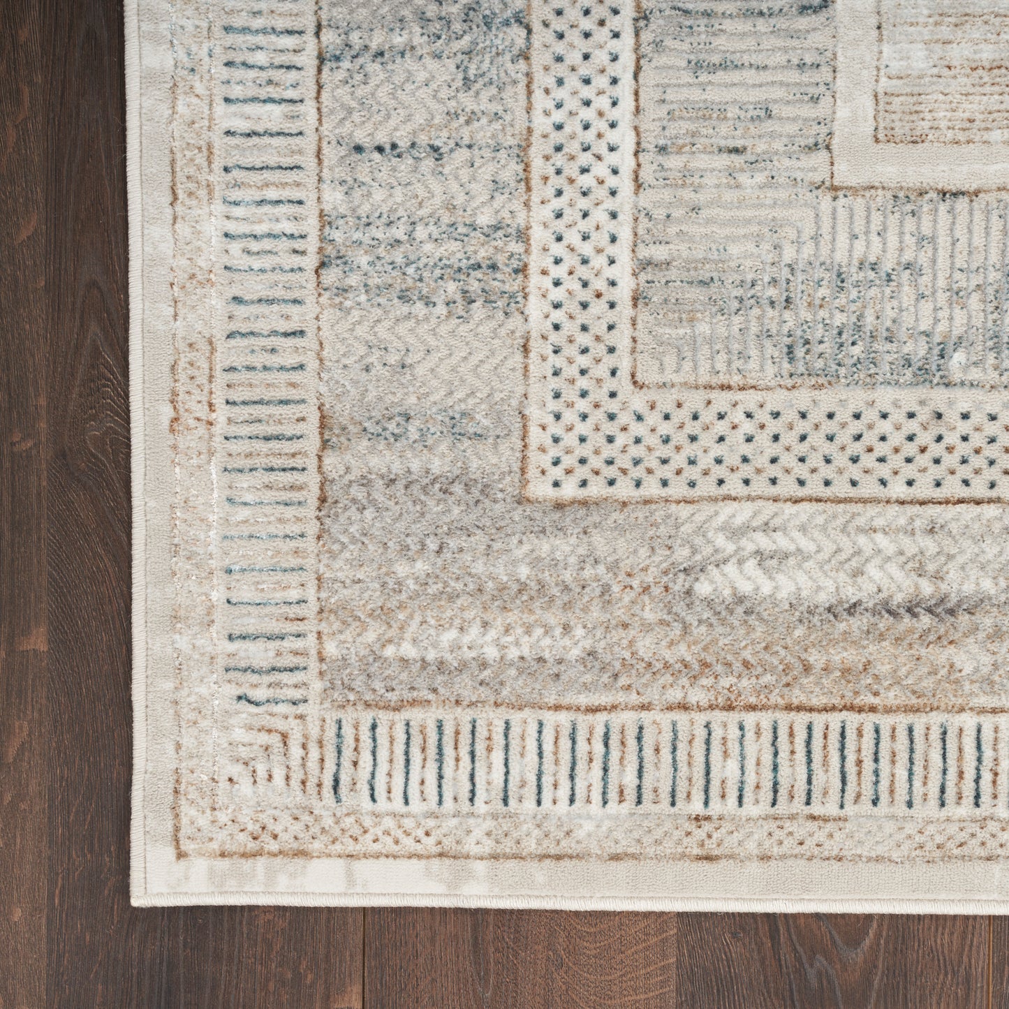 Beige and cream woven area rug with blue stripe accents and geometric border on dark wood floor.