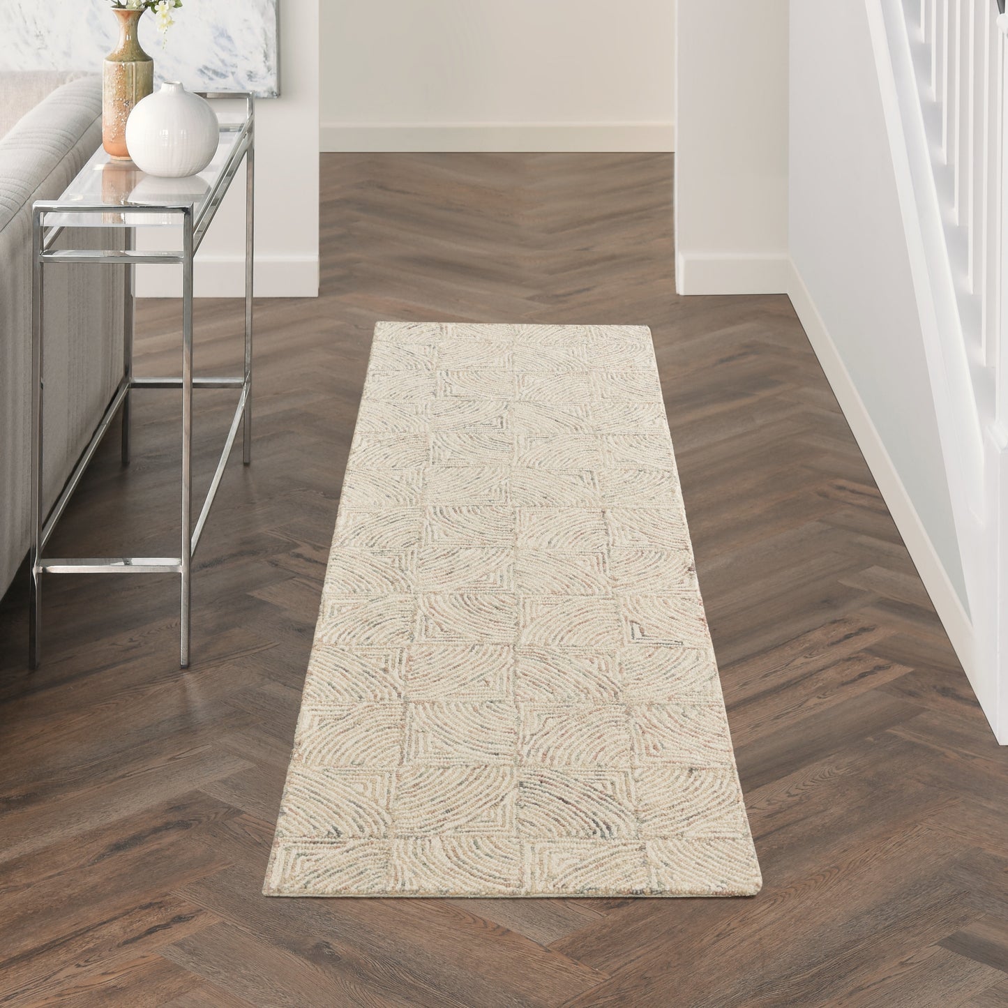 Beige rectangular runner rug with a subtle geometric square pattern on dark wood herringbone floor in a modern hallway.