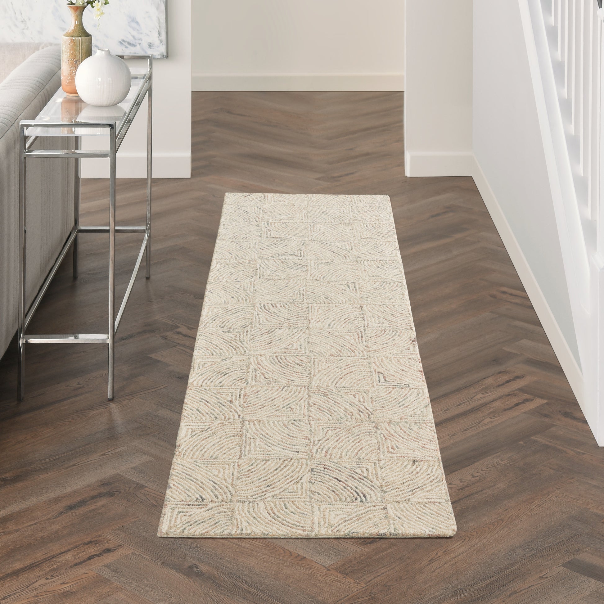 Beige rectangular runner rug with a subtle geometric square pattern on dark wood herringbone floor in a modern hallway.