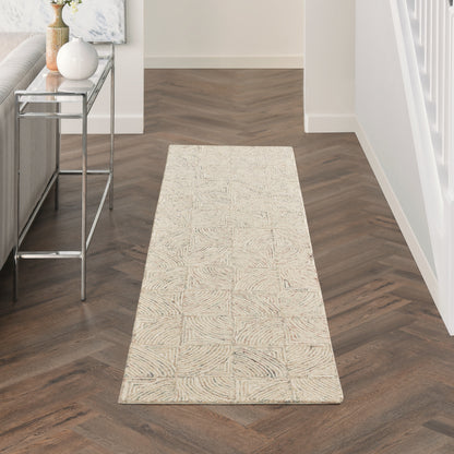 Beige rectangular runner rug with a subtle geometric square pattern on dark wood herringbone floor in a modern hallway.
