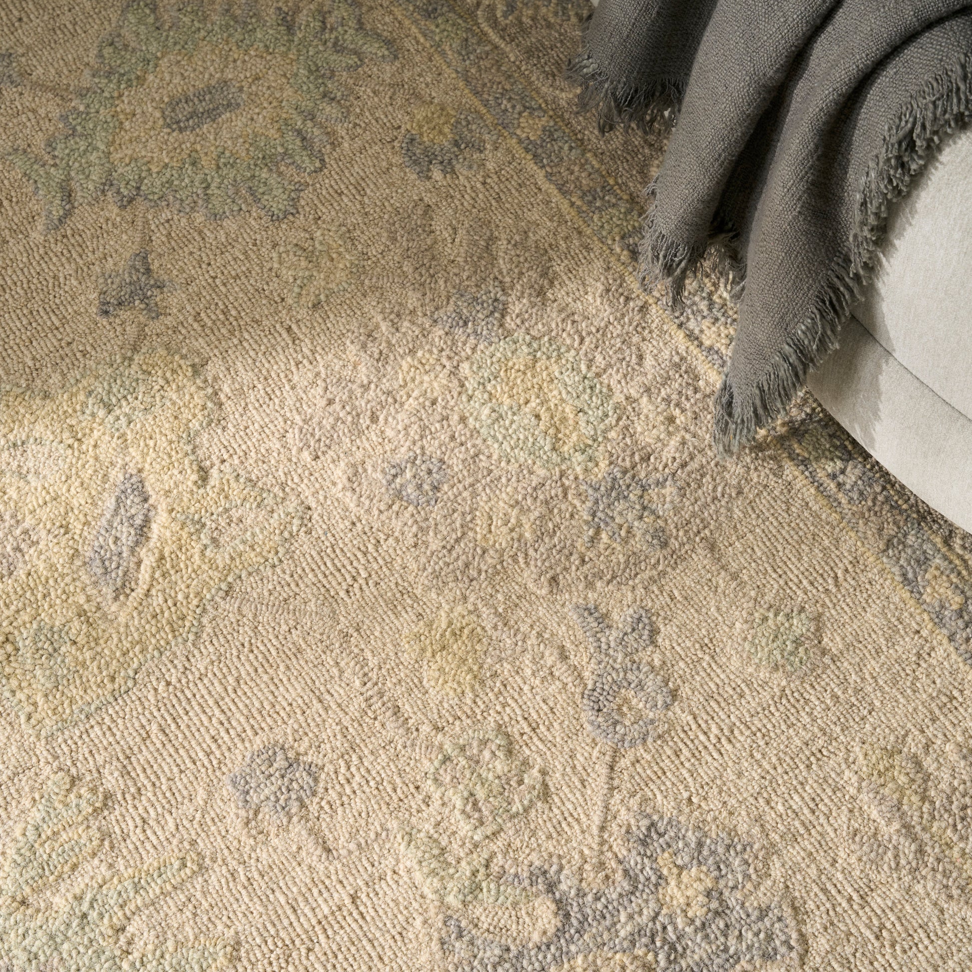 Beige textured oriental rug with gray-blue floral medallions; soft woven pile, with a gray throw blanket.