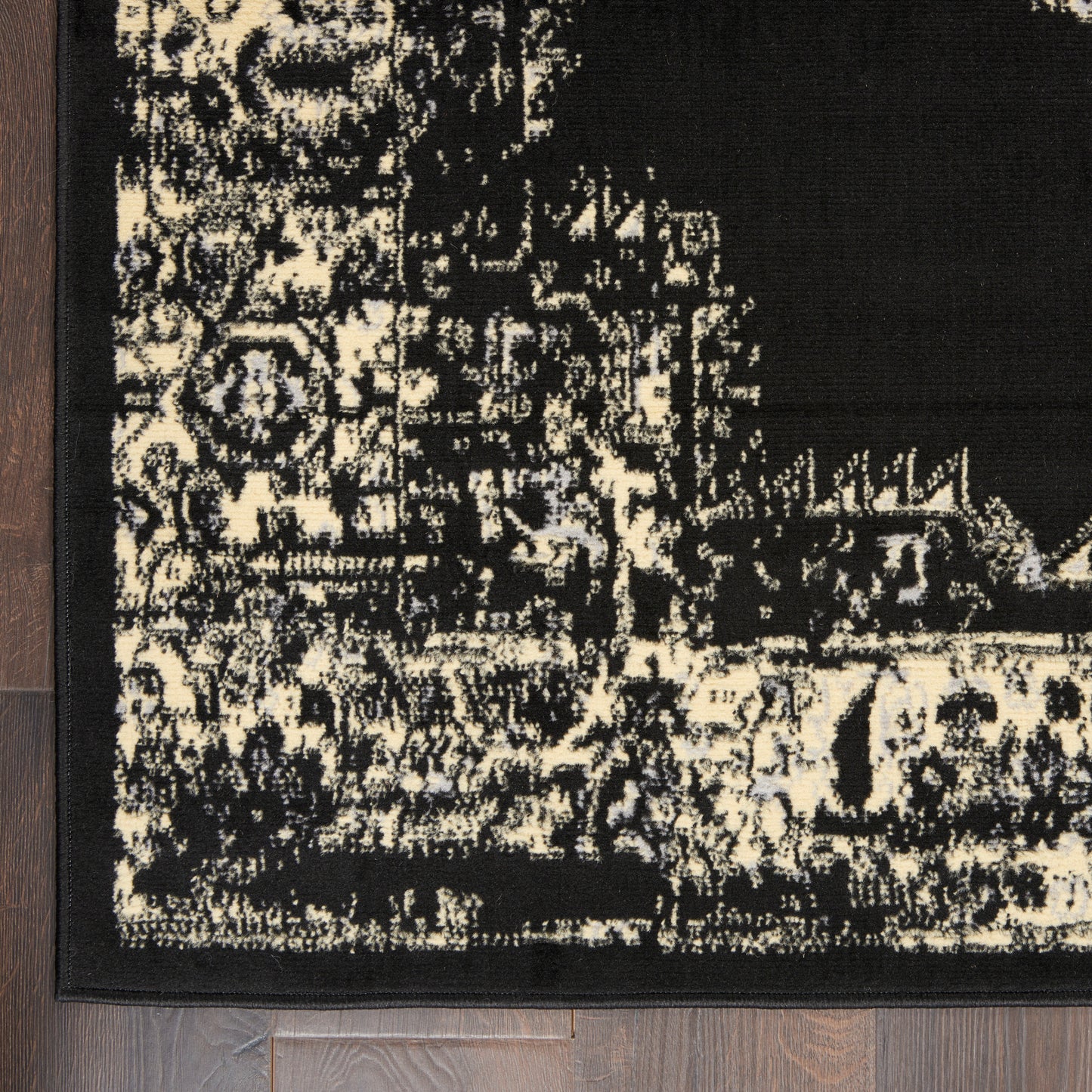 Distressed black-and-cream oriental rug corner with bold border on dark wood floor.