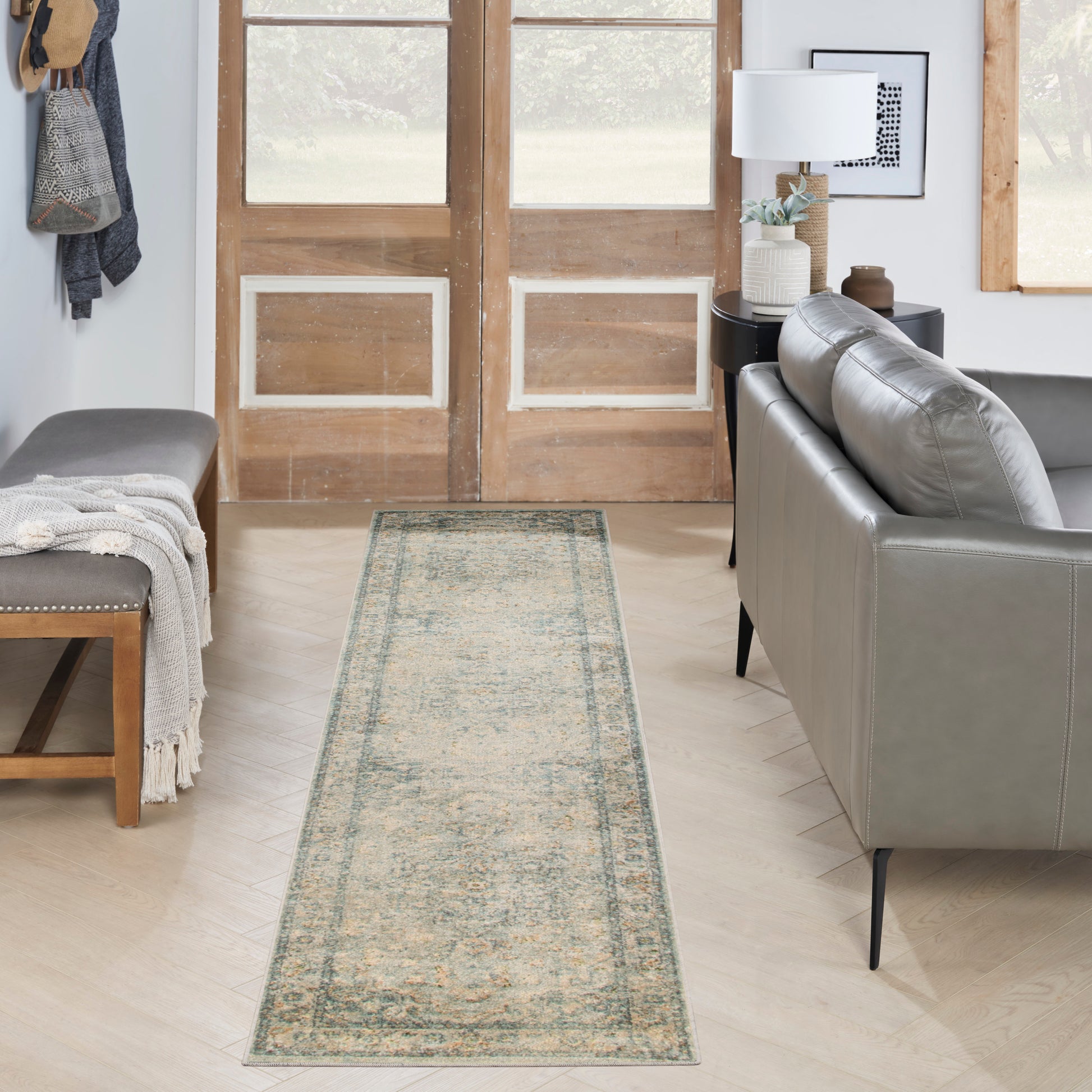 Distressed vintage-style runner rug in muted teal and beige along doorway; grey sofa, wooden bench, throw blanket.