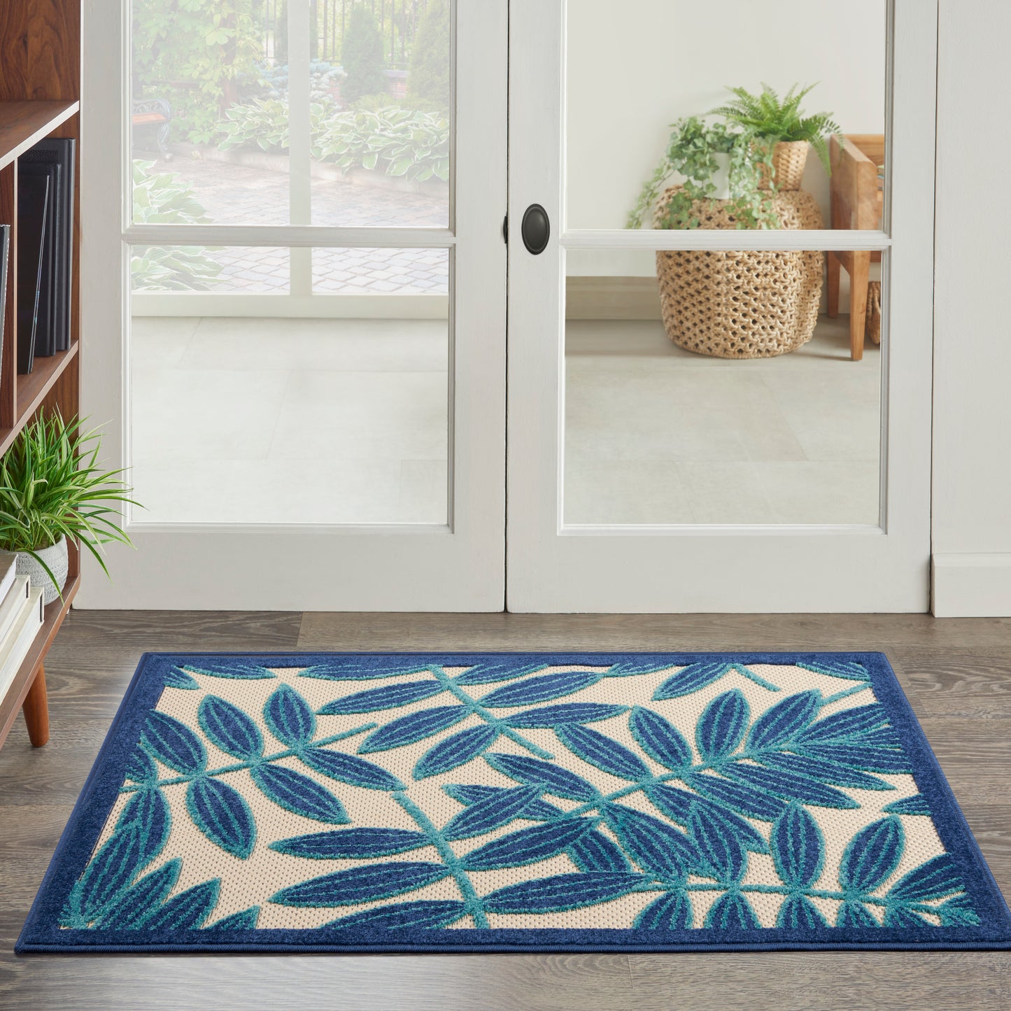 Rectangular doormat with teal-blue tropical leaf pattern on beige background and dark navy border at entryway.