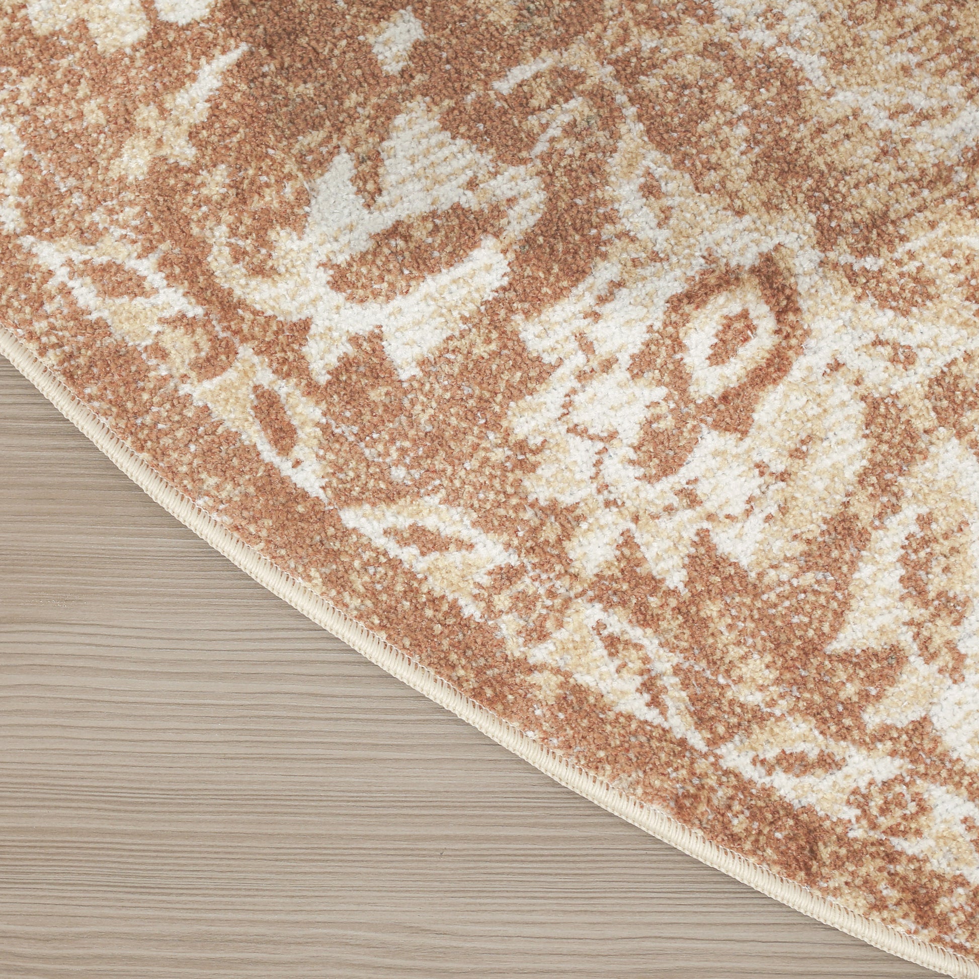 Peach and cream patterned area rug with beige binding edge on light wood floor.
