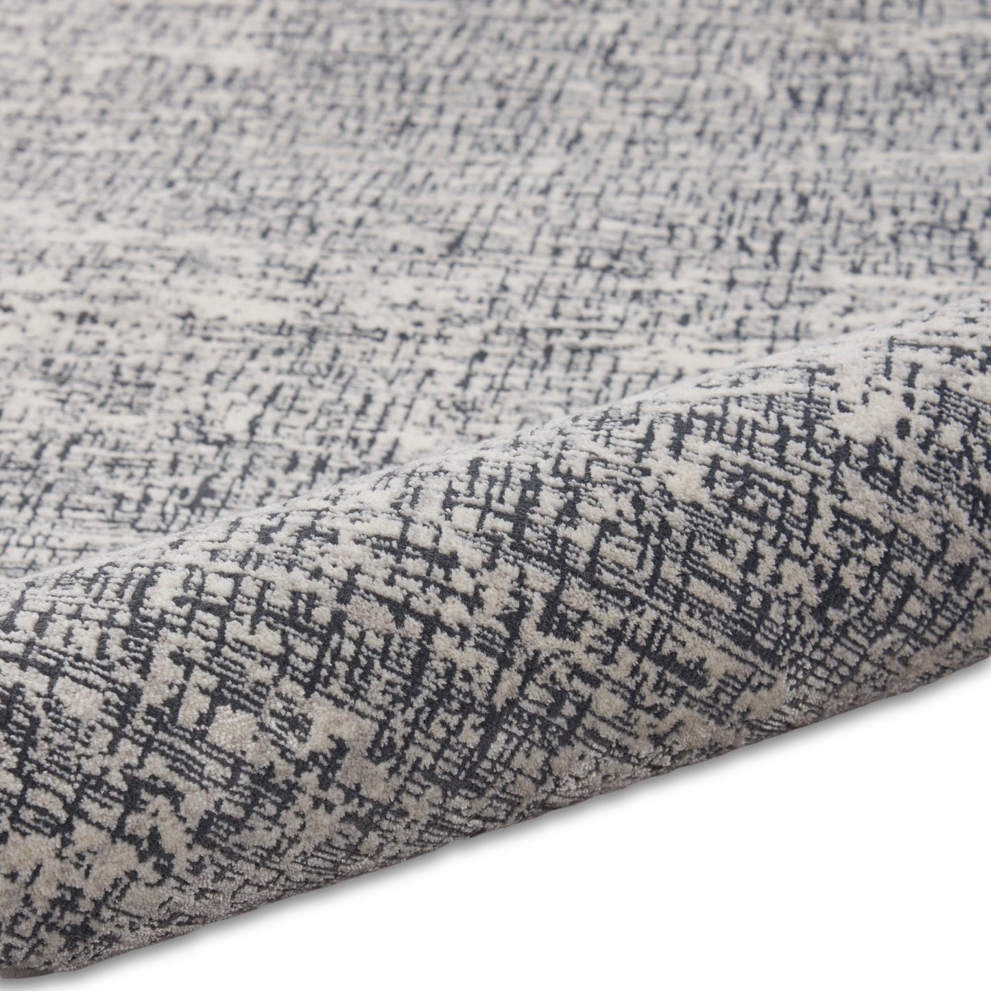 Grey and charcoal abstract patterned rug close-up with folded edge and woven texture.