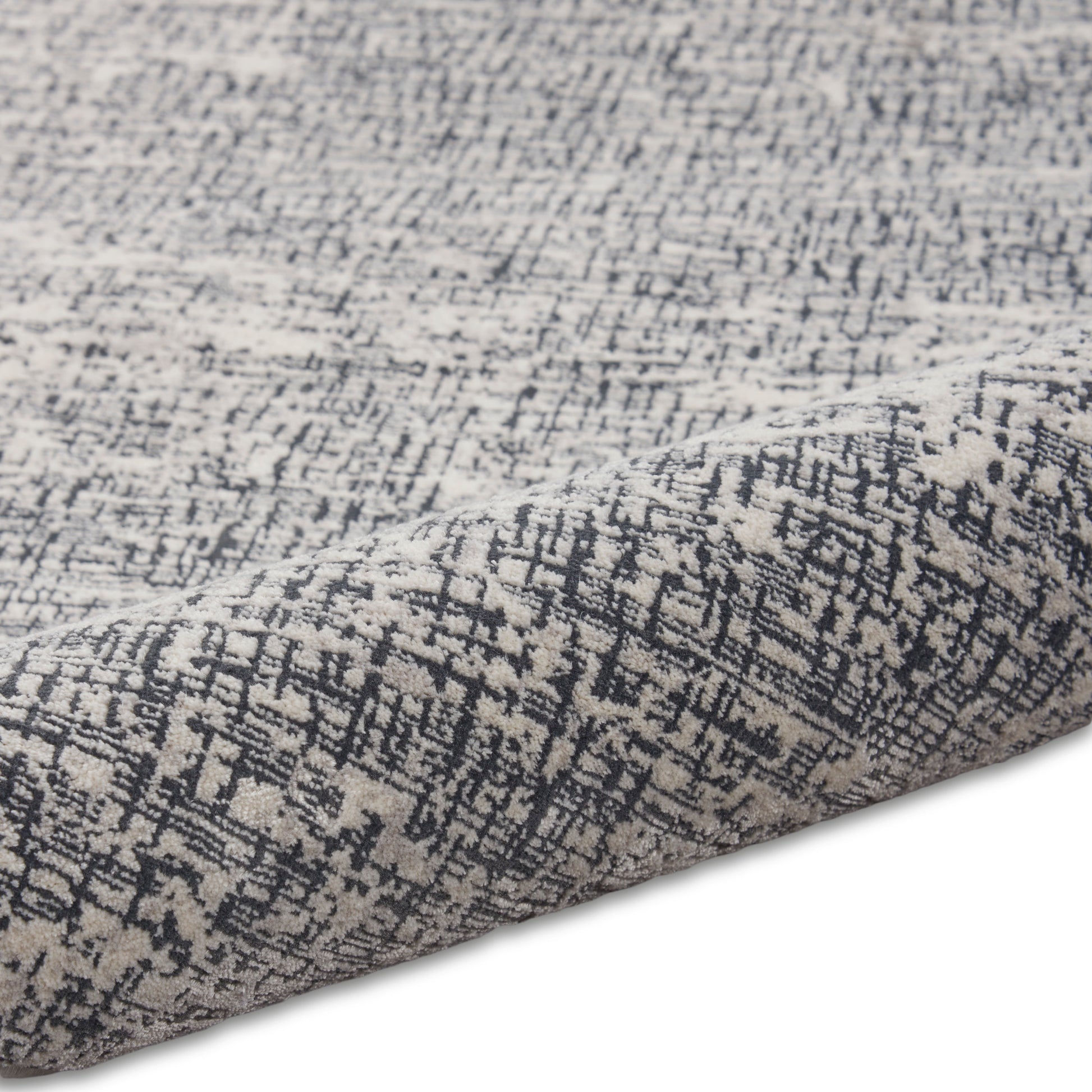 Grey and charcoal abstract patterned rug close-up with folded edge and woven texture.