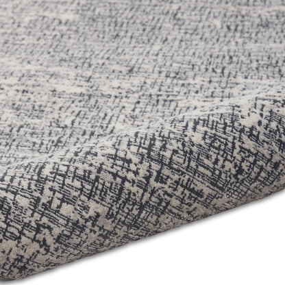 Grey and charcoal abstract patterned rug close-up with folded edge and woven texture.