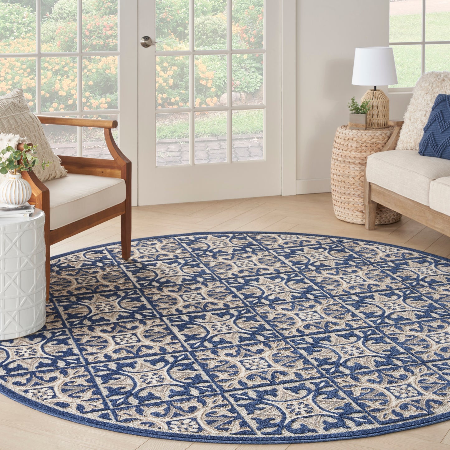 Round blue & beige patterned rug in a bright living room with wicker side table, wooden chair, & glass doors.