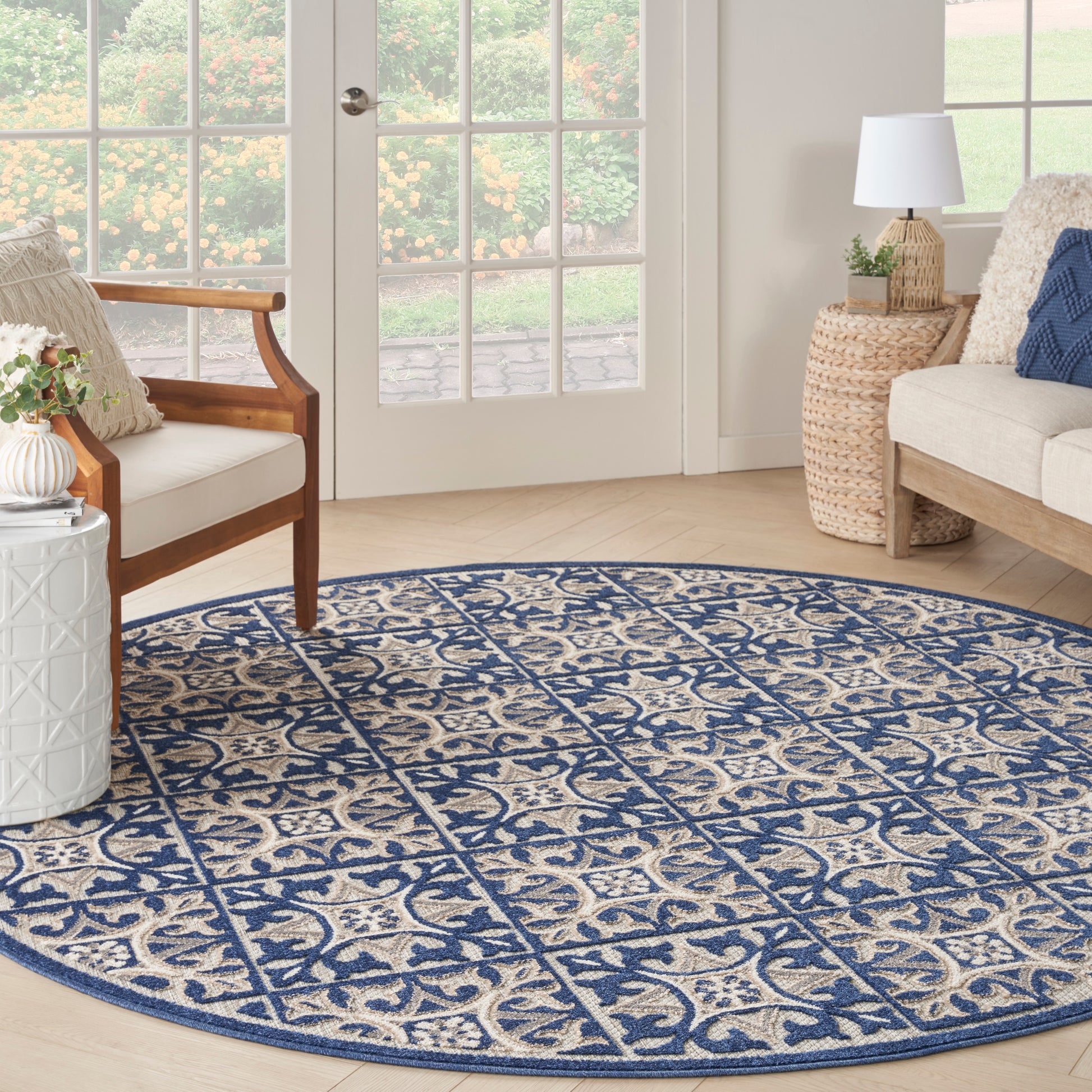 Round blue & beige patterned rug in a bright living room with wicker side table, wooden chair, & glass doors.
