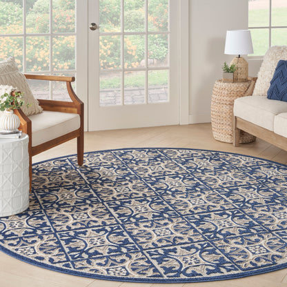 Round blue & beige patterned rug in a bright living room with wicker side table, wooden chair, & glass doors.