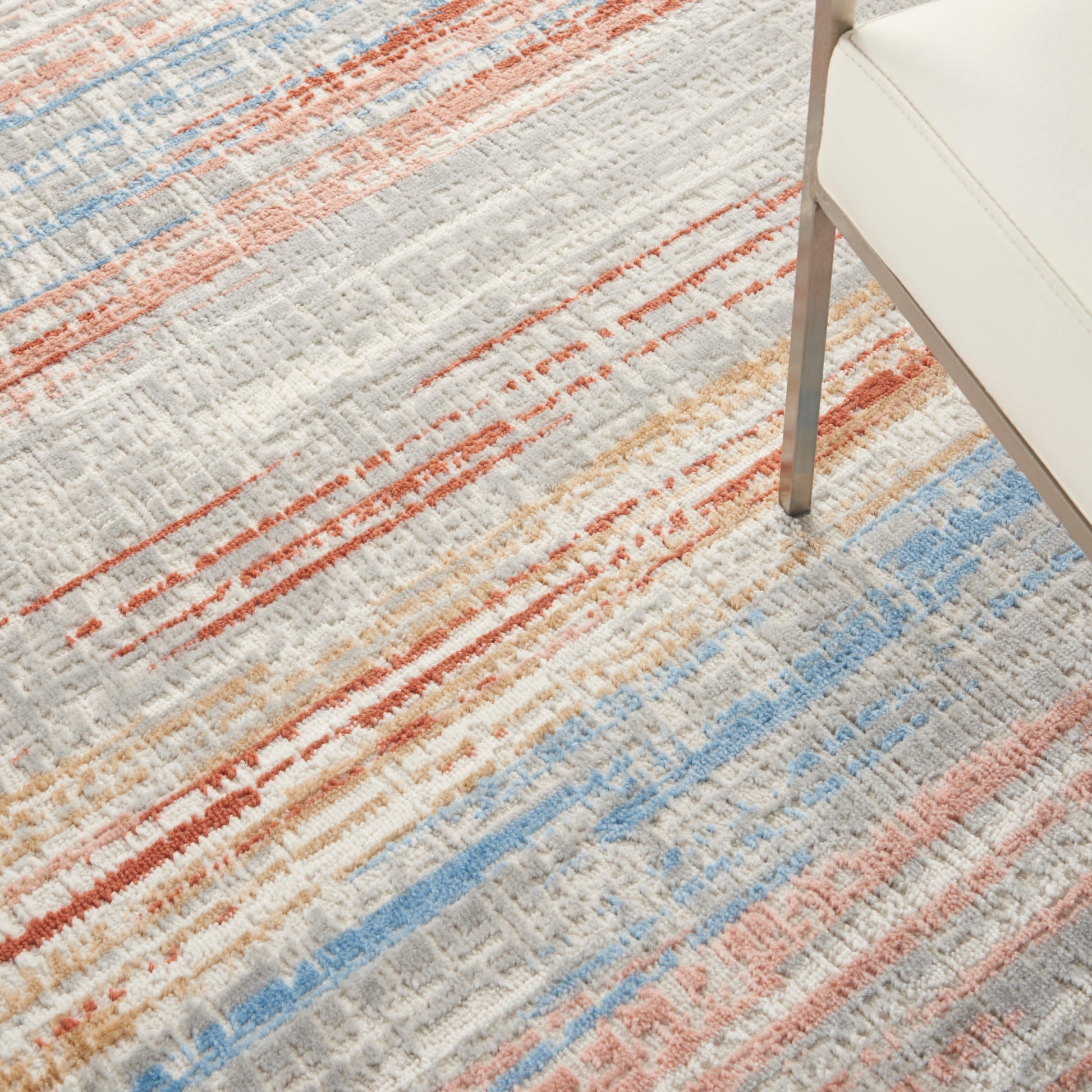 Multicolored abstract striped area rug featuring orange, blue, beige and gray hues; chair leg visible in corner.