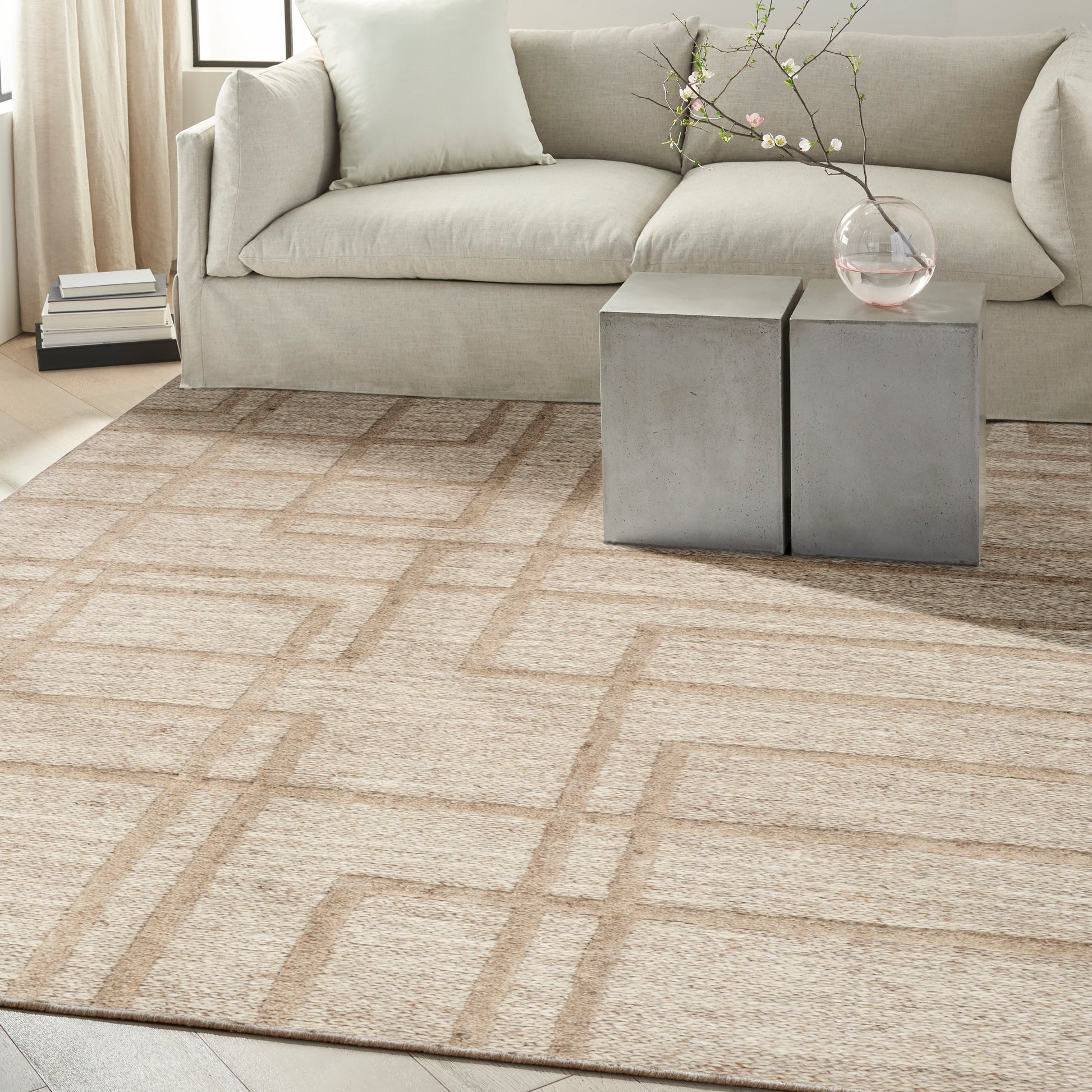 Living room with a beige geometric rug, light gray sofa, and two gray cube side tables with a glass vase and blossom branch.