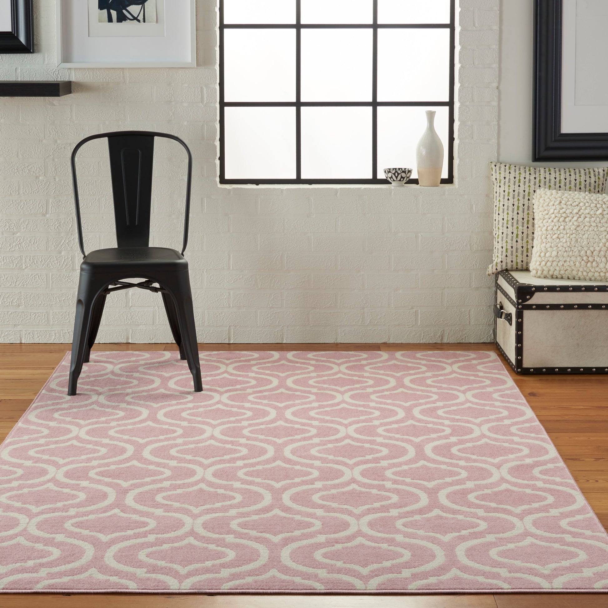 Industrial living room with pink patterned rug, black metal chair, white brick wall, grid window, beige tufted sofa.