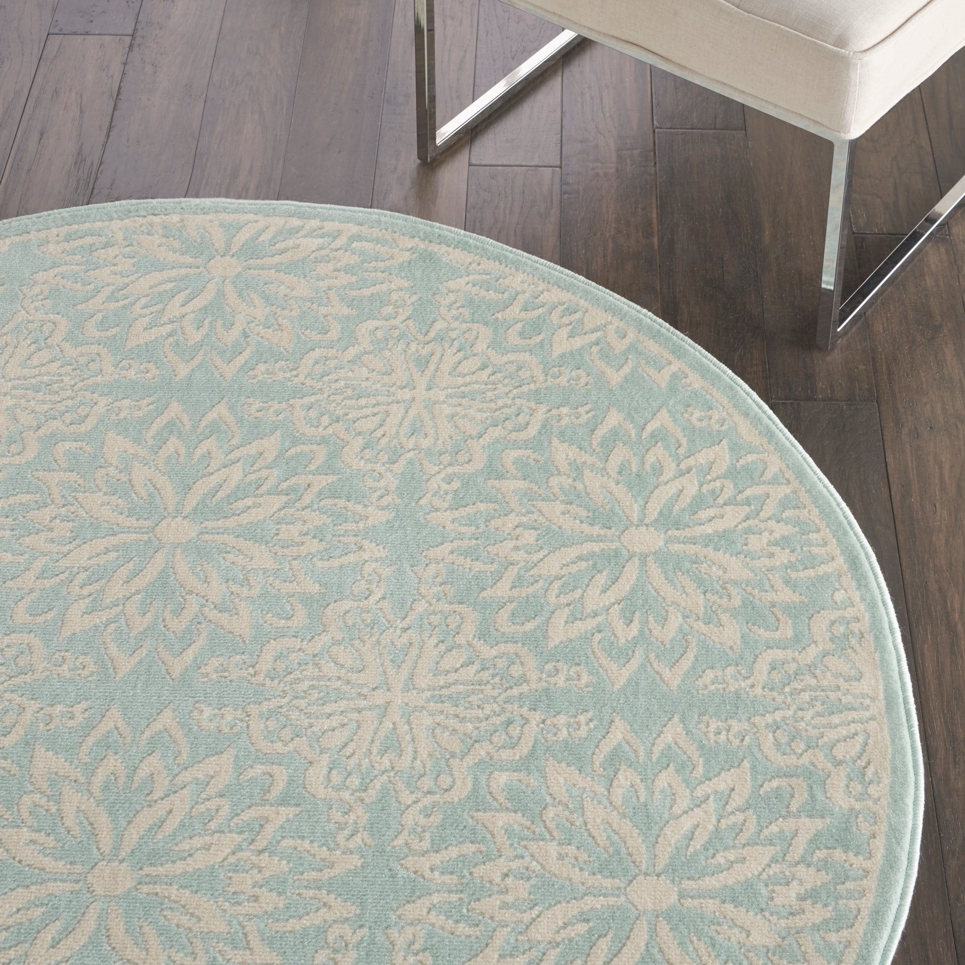 Round light-blue rug with white damask floral pattern and pale border on dark wood floor.