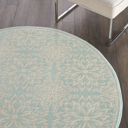Round light-blue rug with white damask floral pattern and pale border on dark wood floor.