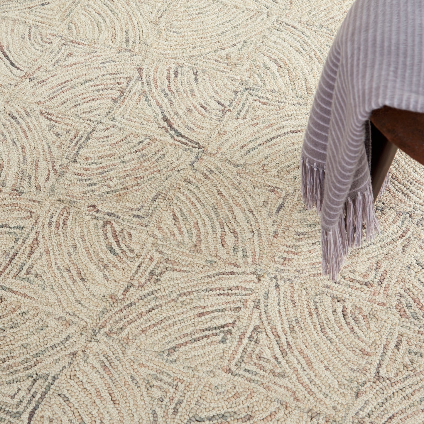 Textured cream rug with beige abstract swirl pattern; lavender fringed throw draped over a chair.