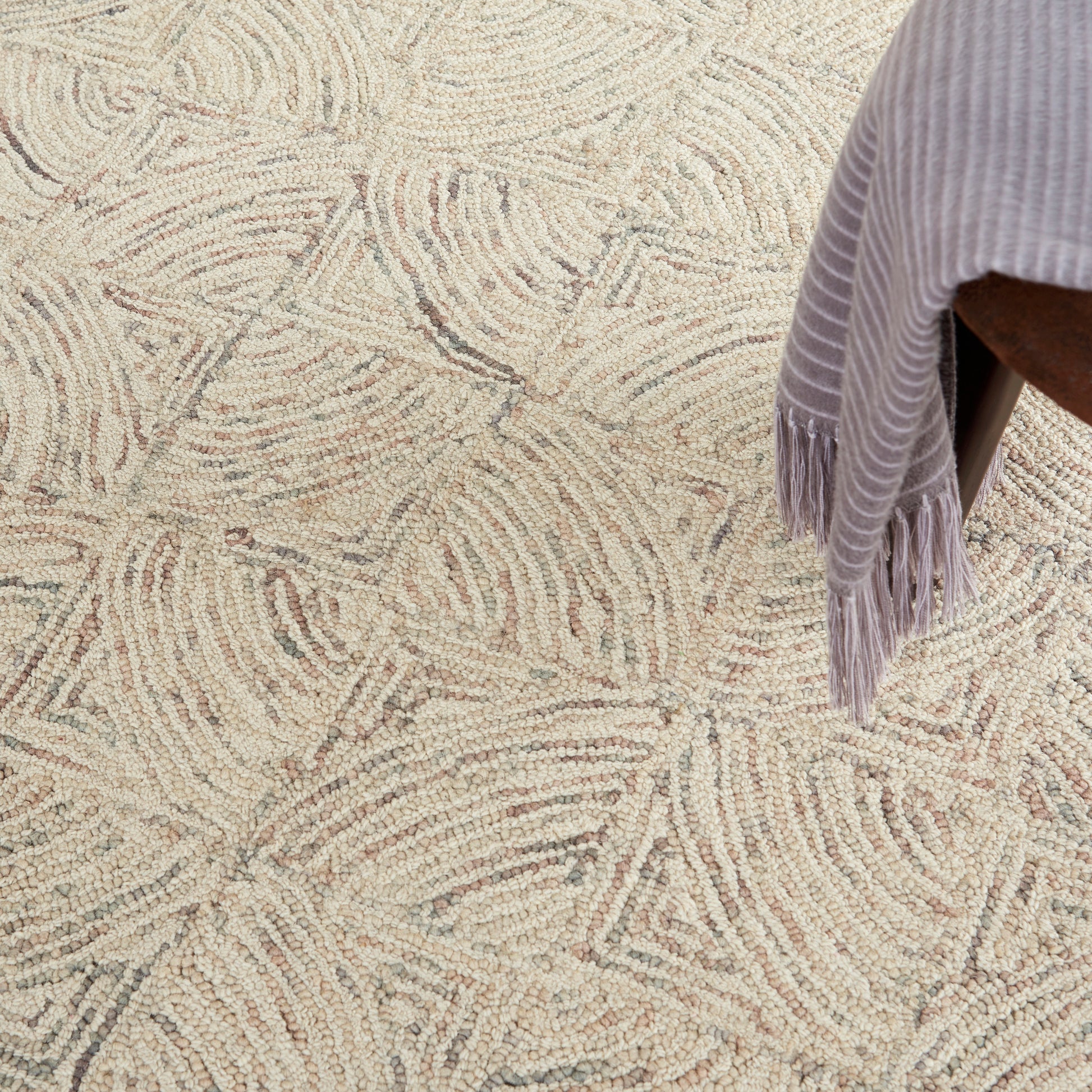 Textured cream rug with beige abstract swirl pattern; lavender fringed throw draped over a chair.