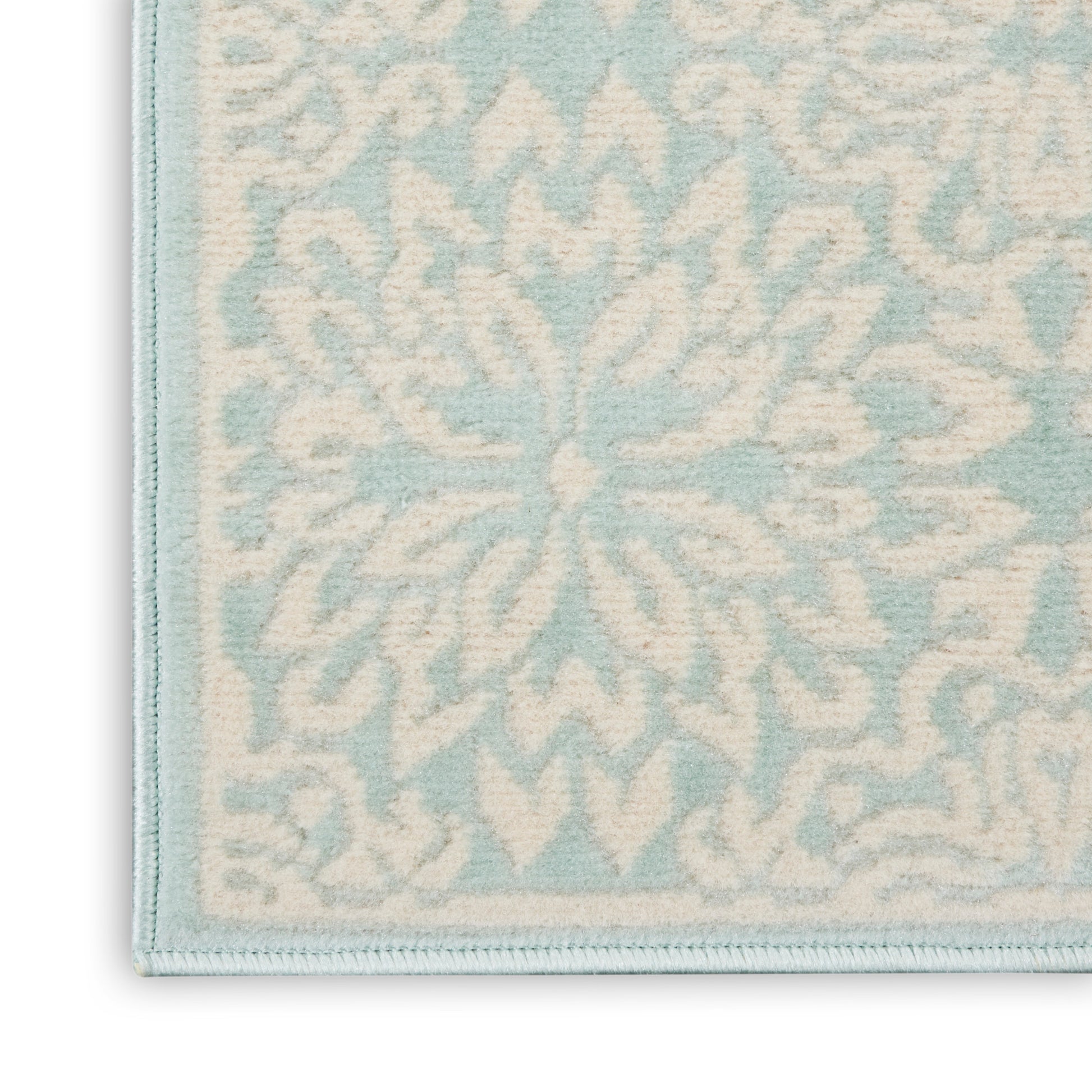 Close-up of pale blue & cream woven rug with a snowflake floral pattern and light blue border.