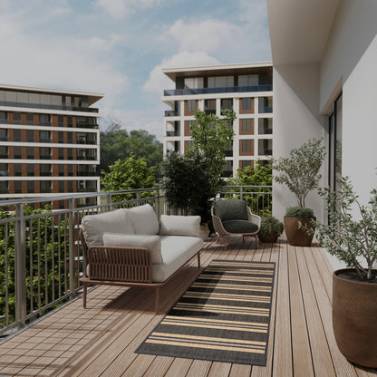 Modern balcony with wooden deck, beige cushioned rattan sofa, dark lounge chairs, striped runner rug, and potted plants.