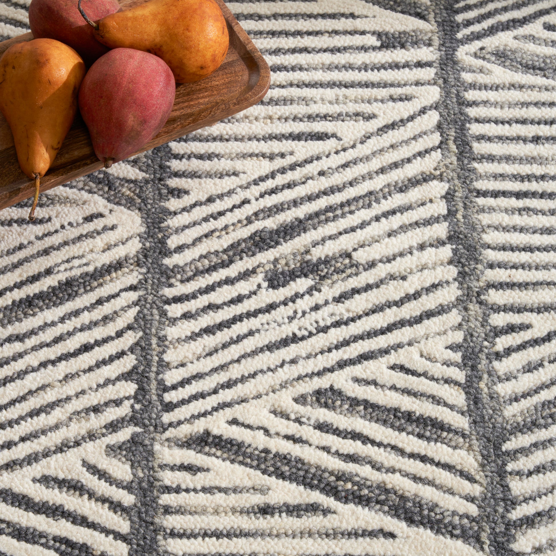 Brown wooden tray with orange-red pears sits on a cream and charcoal geometric woven rug.