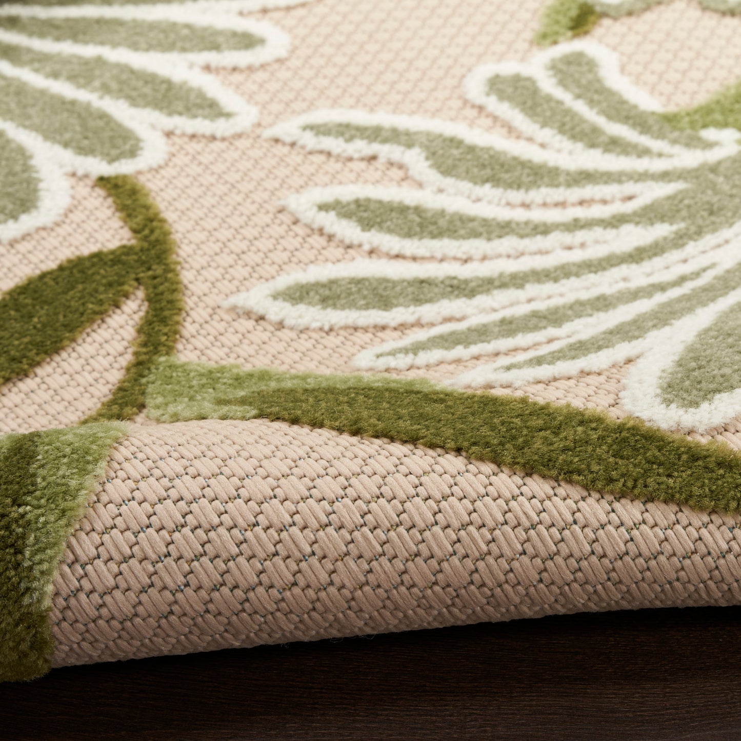Beige-pink woven rug with green palm leaf pattern, soft loop texture, bound edge on dark wooden floor.