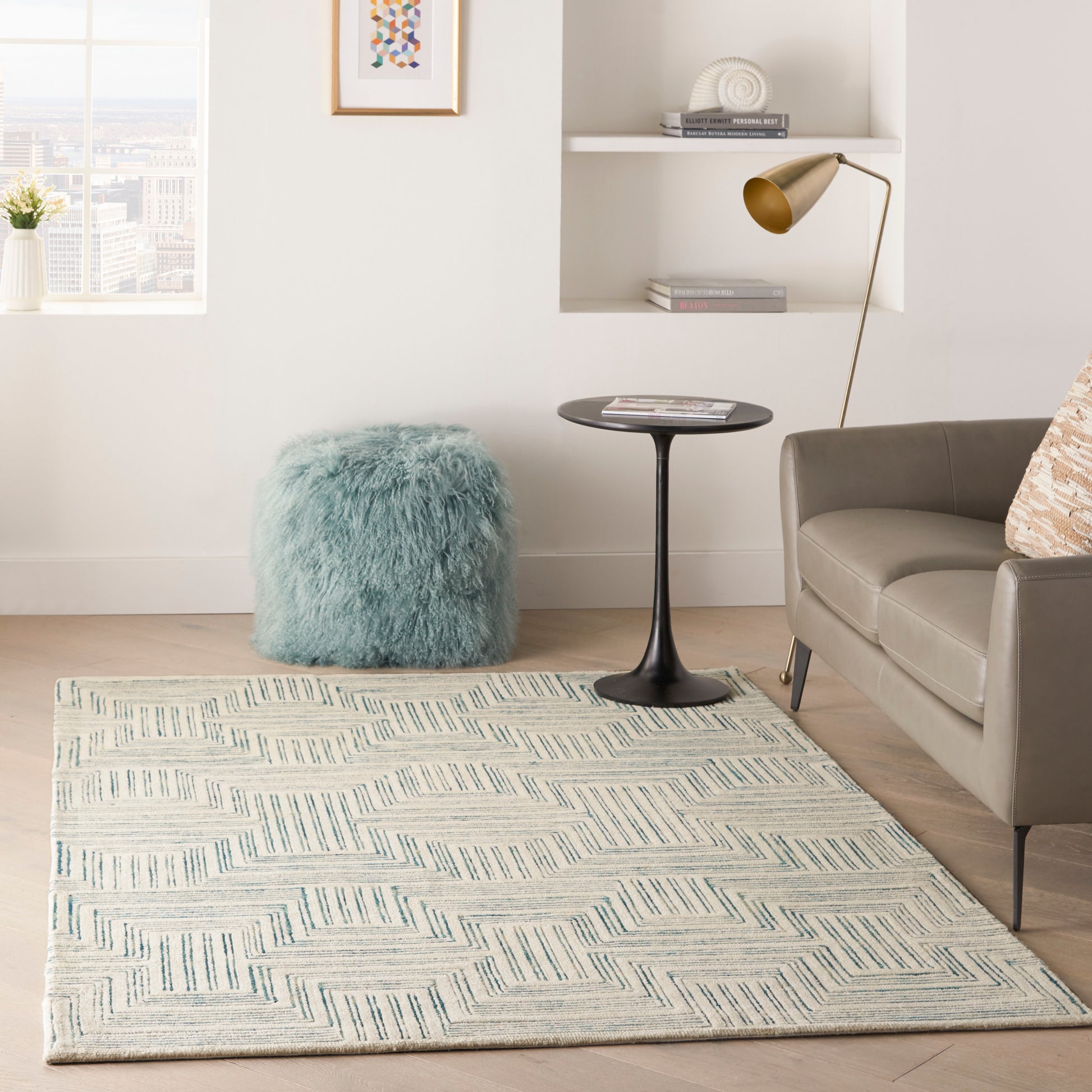 Blue geometric rug (4' x 6') in a cozy living room corner with a beige sofa, black round side table, brass floor lamp, and teal fluffy pouf.