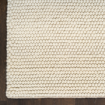 Cream textured loop rug on dark wood floor; close-up of tight knobby loops.