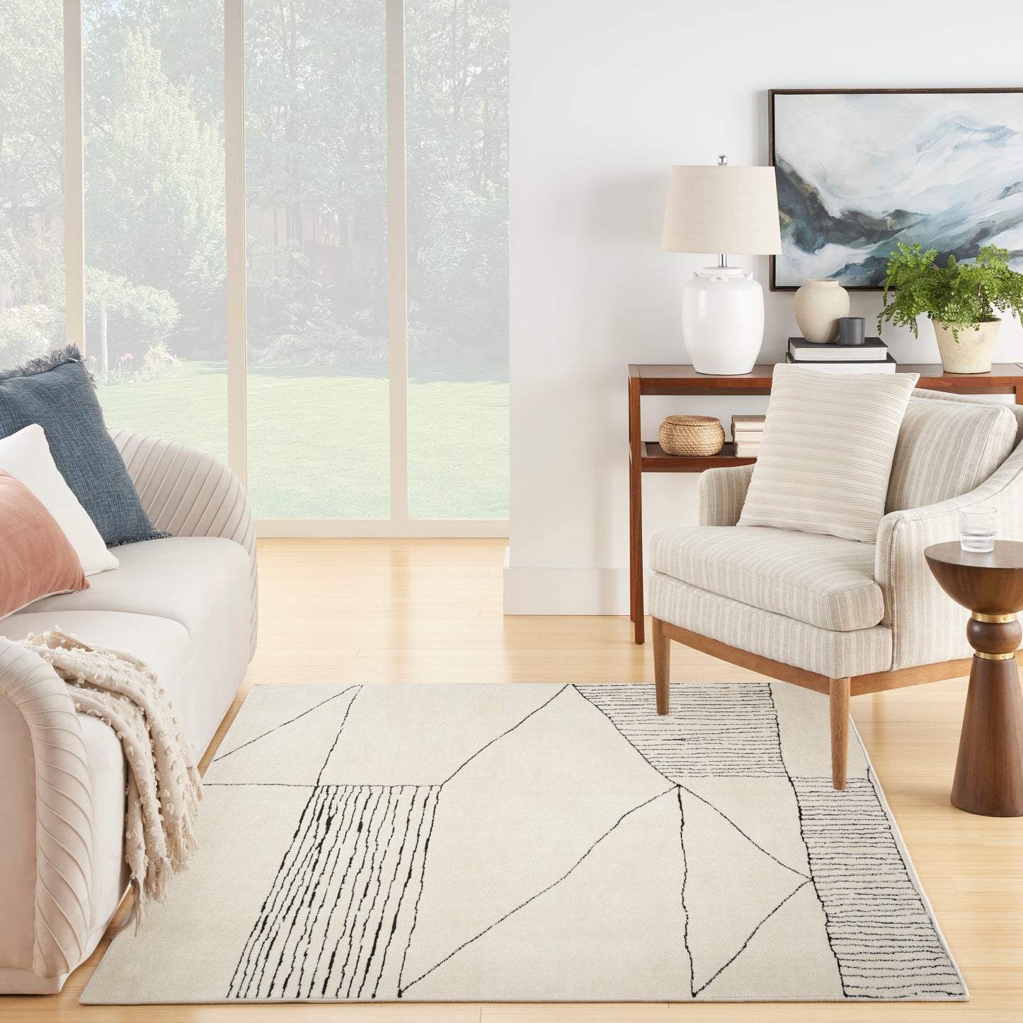 Neutral living room with geometric beige area rug featuring black linear shapes, cream sofa, wood chair, and large windows.