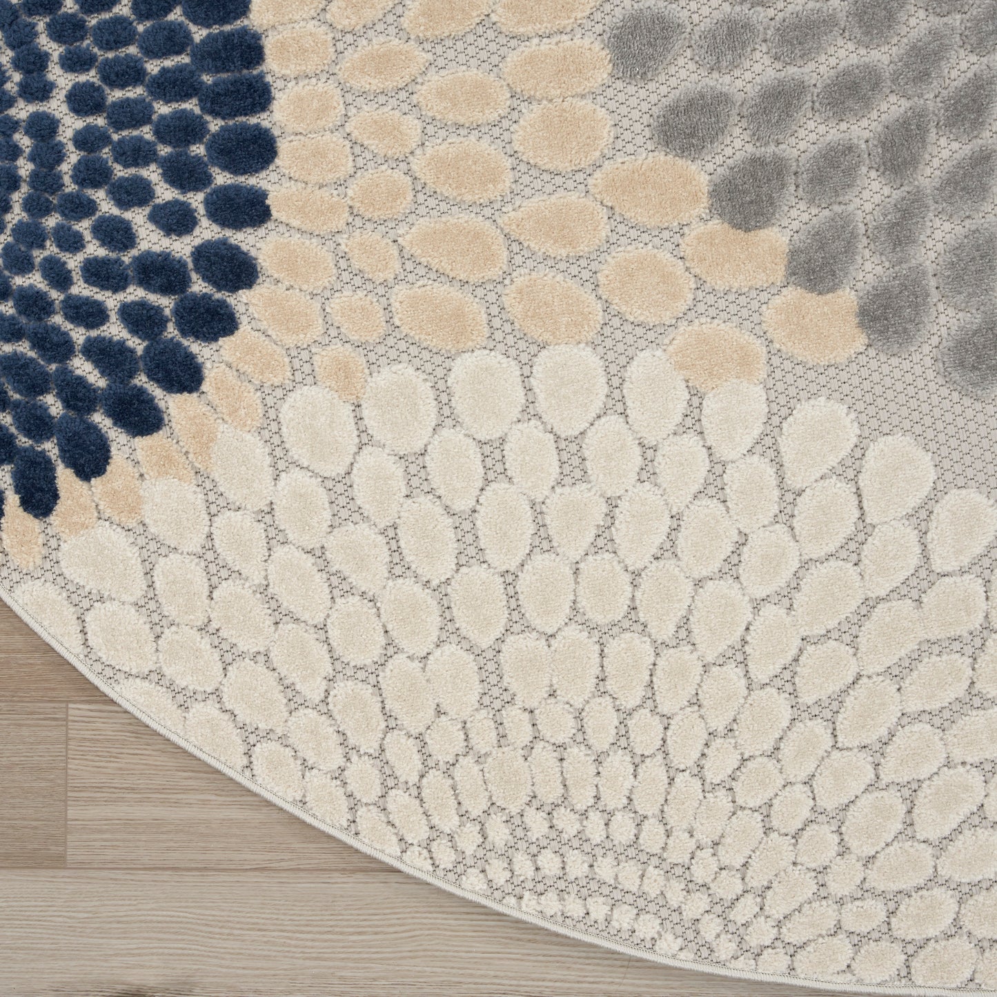 8' round rug with pebble-pattern in navy, beige, taupe and cream; textured woven design on light background; modern coastal style.