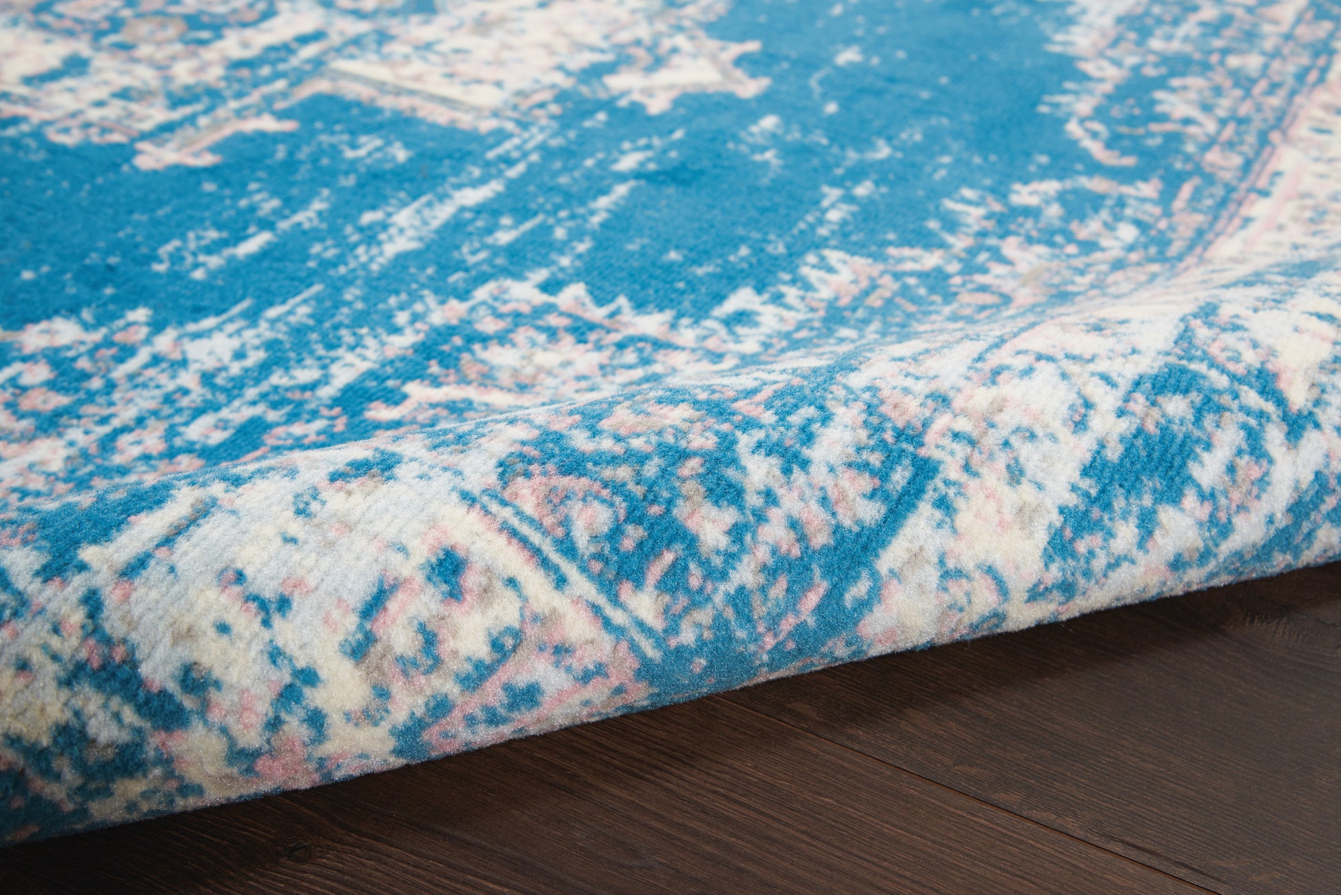 Blue area rug with pink & white distressed pattern, rolled edge on dark wood floor