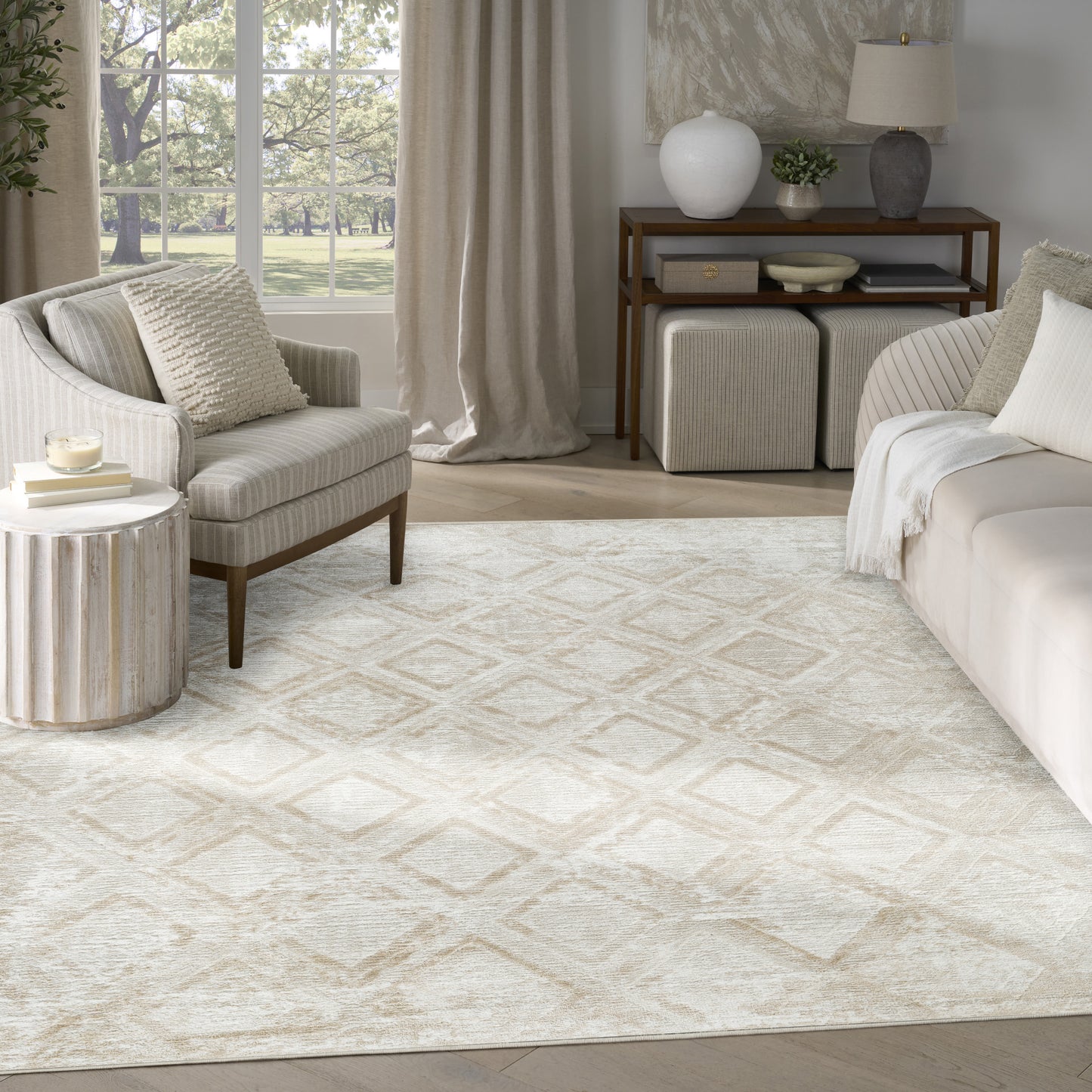 Neutral living room with cream sofa, striped armchair, geometric beige rug, wooden side table, ottomans, and greenery.