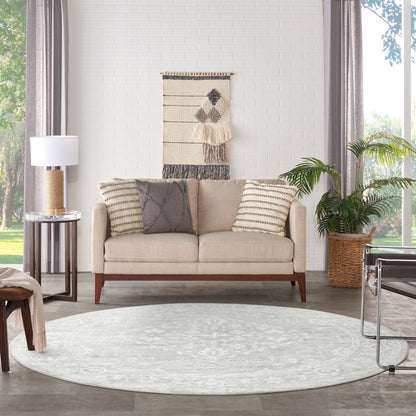 Beige tufted sofa with striped and quilted cushions, round grey rug, woven wall hanging, and potted plant in living room.