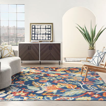 Bright living room with blue floral rug, gray sofa, dark wood mid-century sideboard, abstract art, wicker chair and plant.