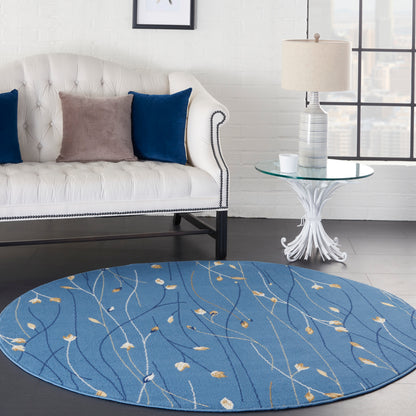 Round blue rug with cream floral vines under a white tufted sofa; navy and taupe pillows, glass side table, striped lamp.