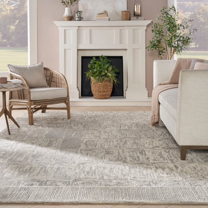 White paneled fireplace in a neutral living room with beige sofa, wicker chair, gray patterned rug, and potted greenery.