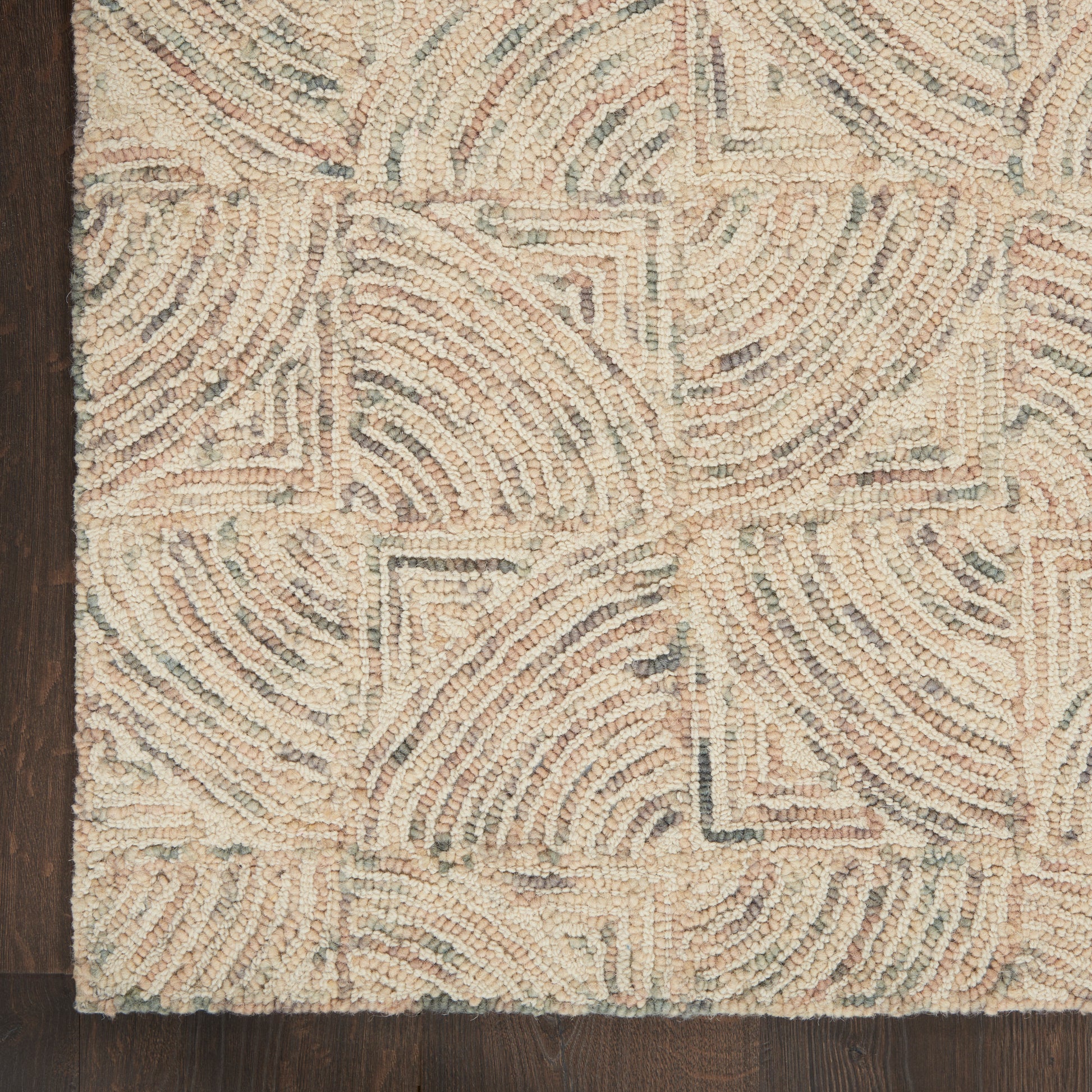 Beige looped-wool rug with swirling arc patterns and geometric square motifs on dark wood floor.