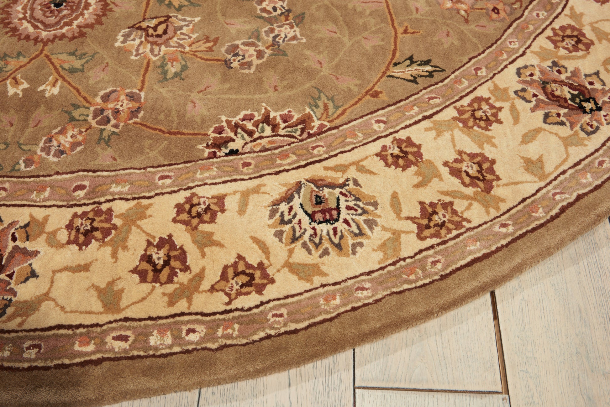 Round Oriental floral rug in beige, cream, tan and burgundy on a light wood floor.