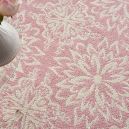 Soft pink rug with white floral/mandala patterns; round glass coffee table edge visible.
